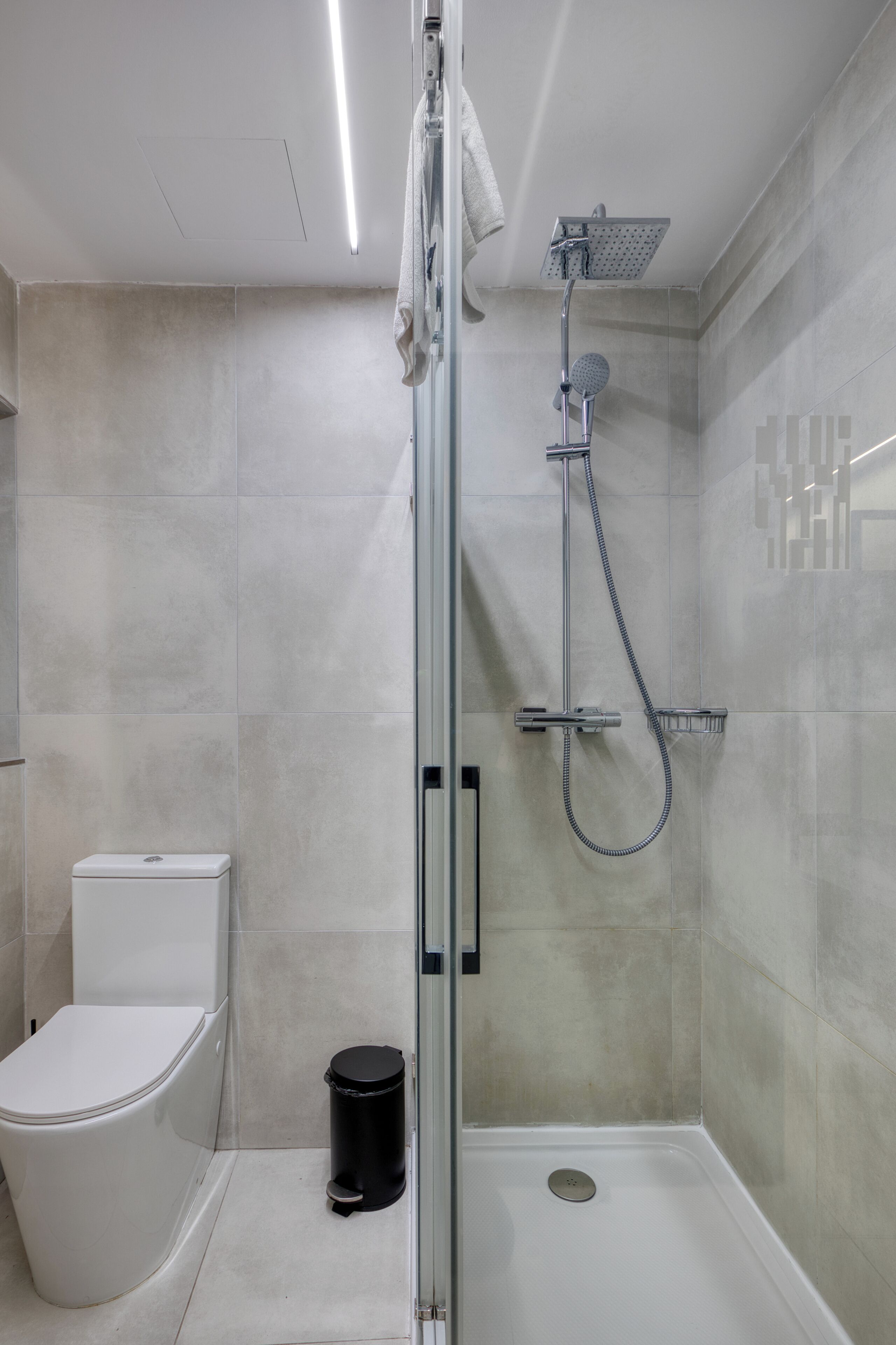 A modern bathroom with a glass-enclosed shower, a toilet, and a trash bin.