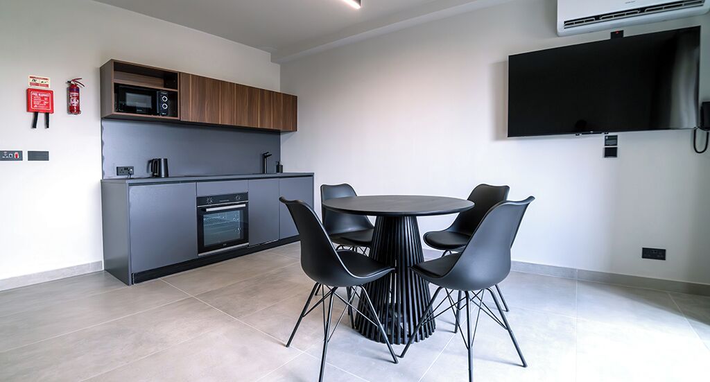 A modern kitchen with a microwave, oven, and built-in cabinets. There is a dining area with a round table and four chairs. A flat-screen TV is mounted on the wall.