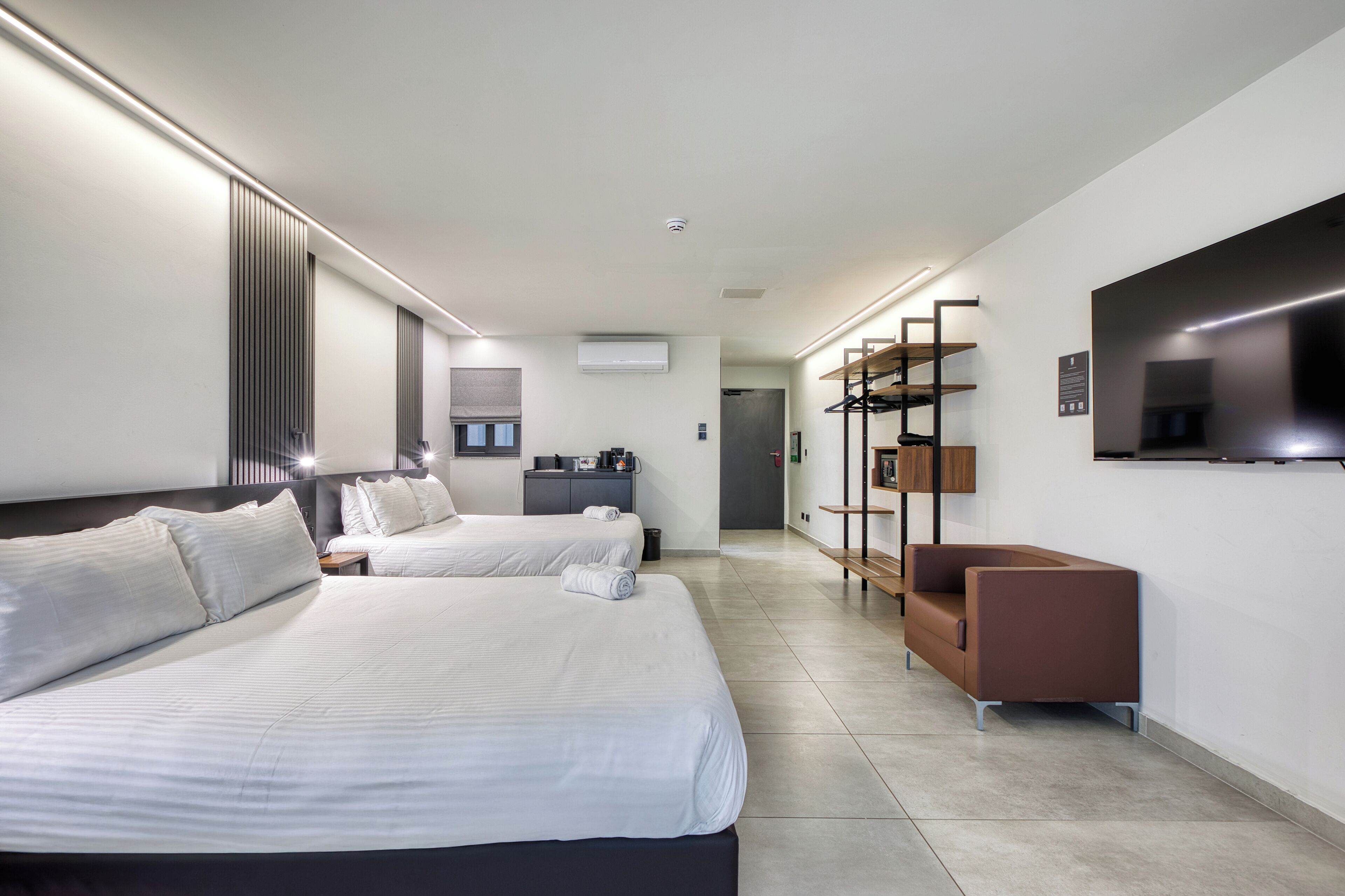 A modern hotel room with two beds, a sofa, a TV, and a wardrobe.