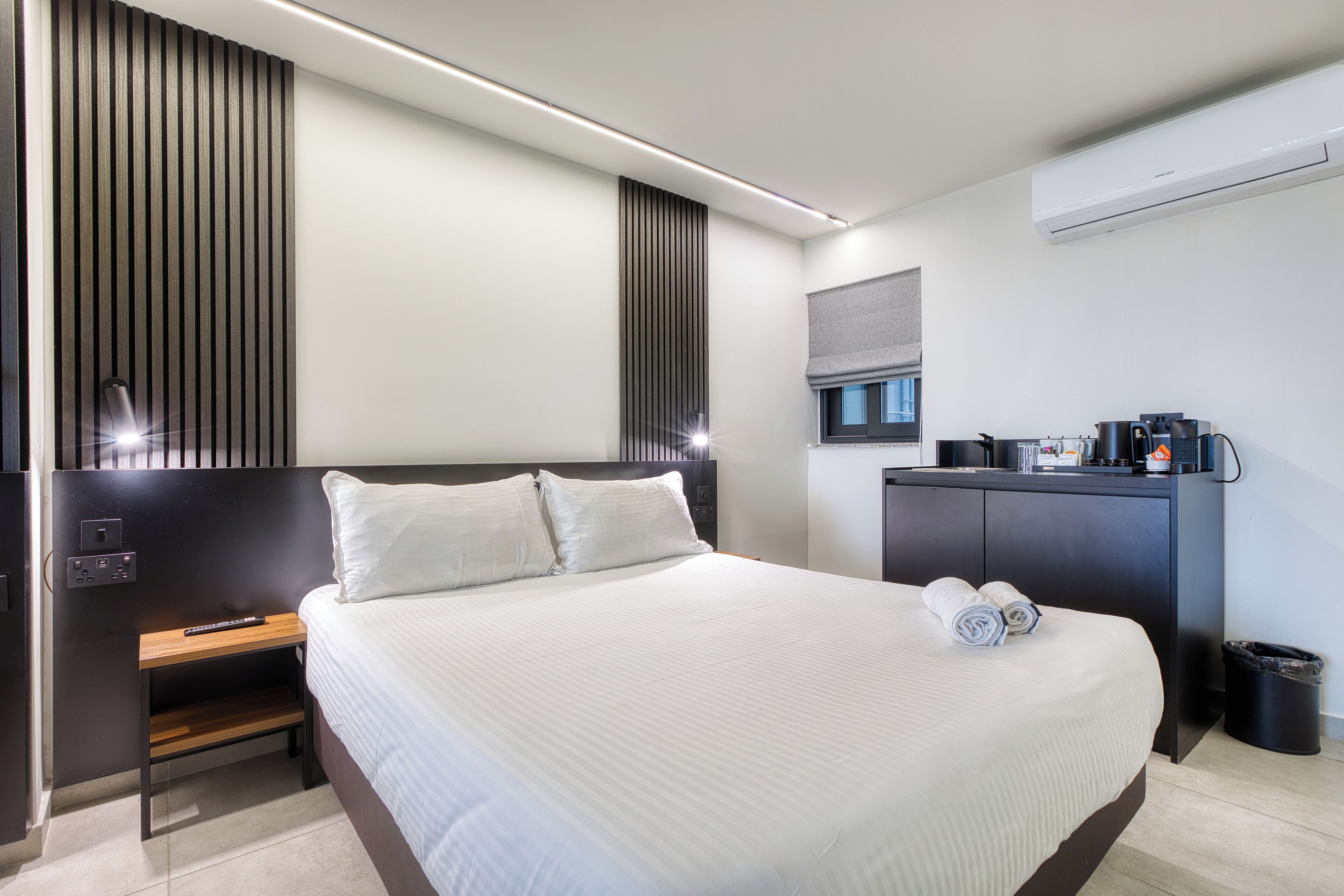 A modern hotel room with a large bed, a wooden nightstand, a desk with a computer, and a small seating area.