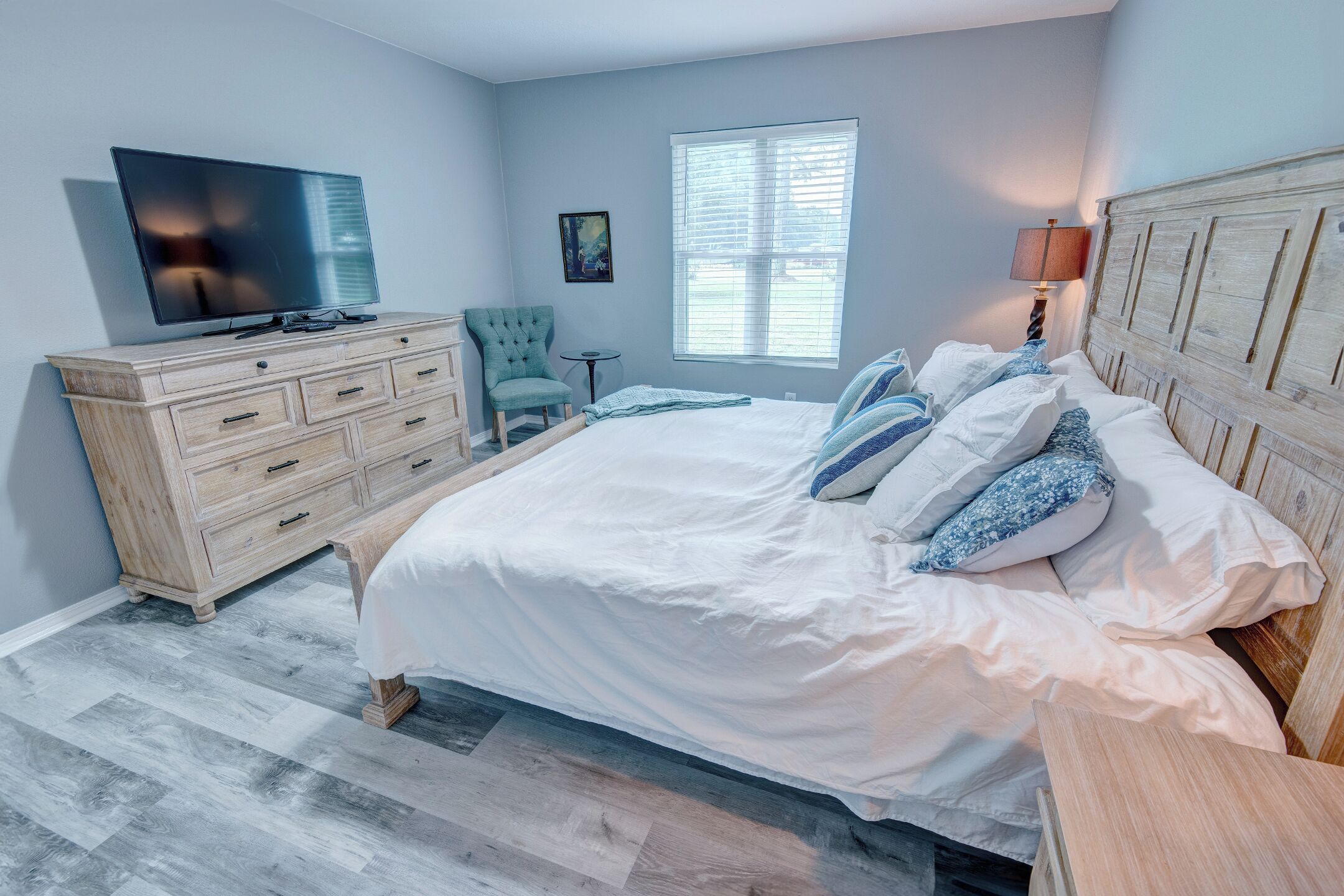 A bedroom with a bed, a TV, a dresser, a chair, and a window.