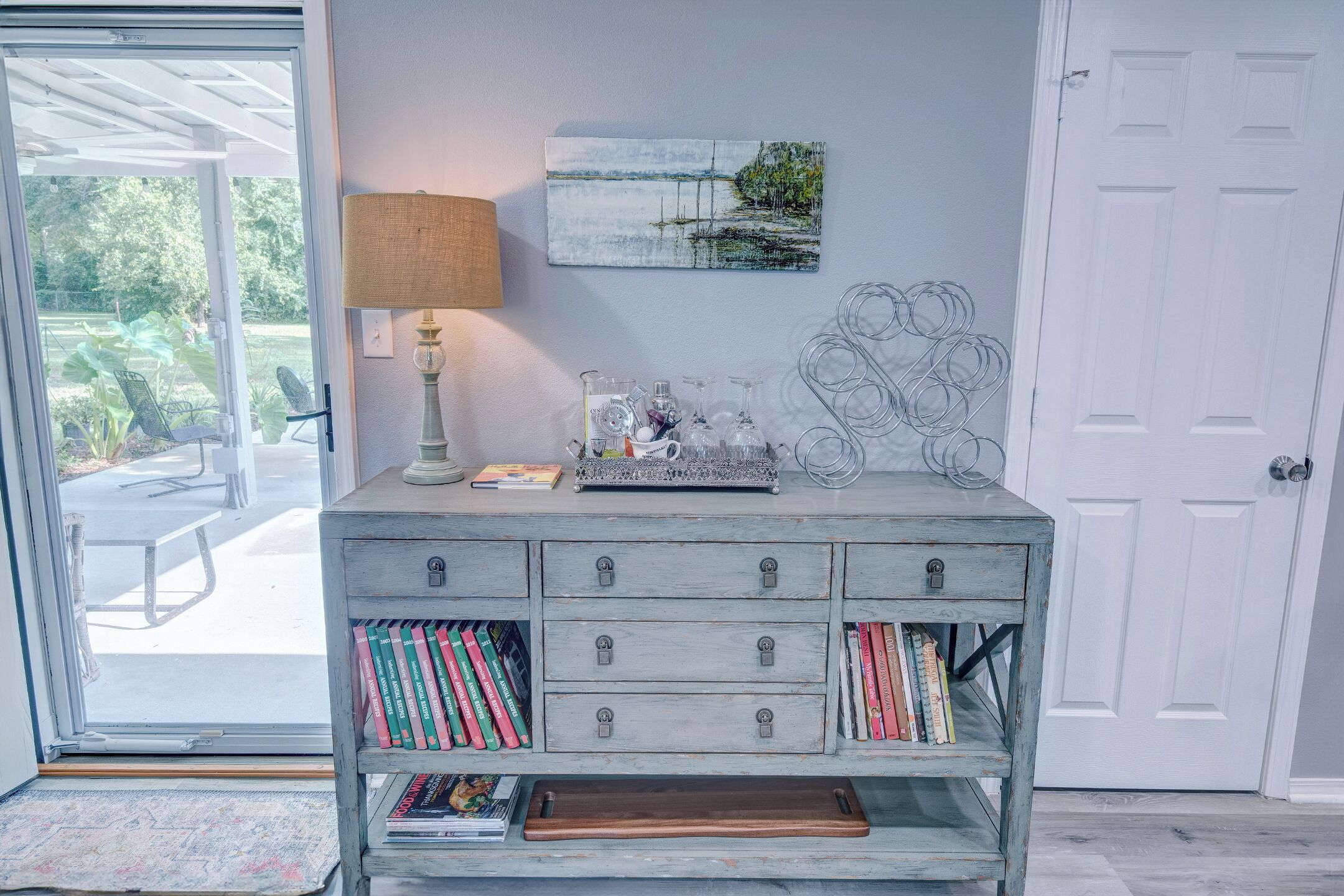 Quarto com cômoda de madeira, luminária, pintura e porta.