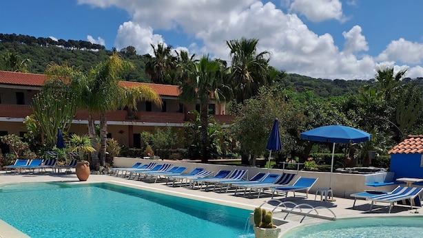 A resort pool area with clear blue water, lounge chairs, and umbrellas. -  Agriturismo Heaven (Ricadi)