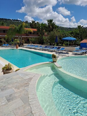 Un espace piscine aménagé dans un complexe hôtelier, avec une eau d’un bleu limpide, des chaises longues et des parasols.