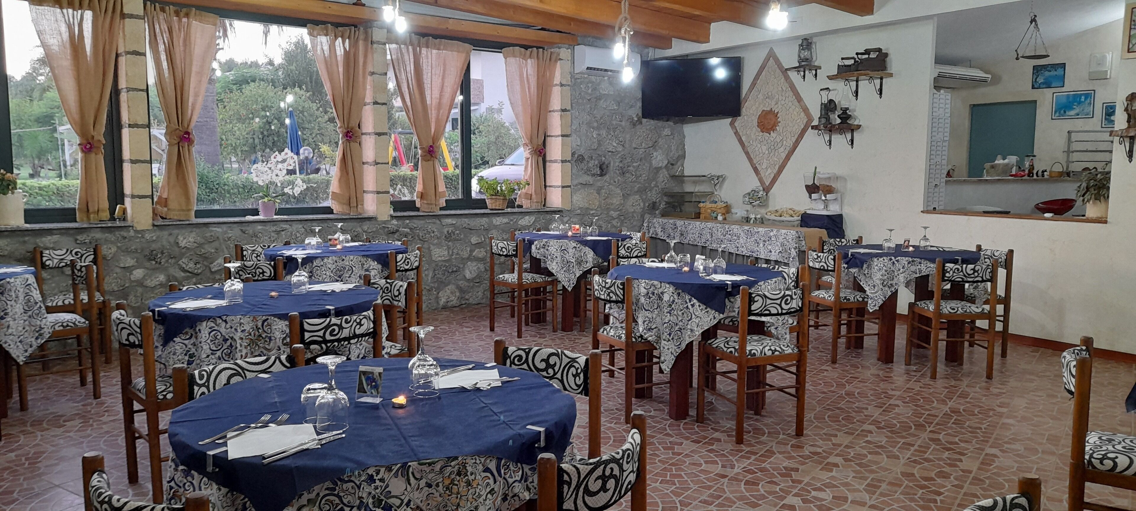 A restaurant with round tables covered with blue tablecloths, wooden chairs, and a stone wall.