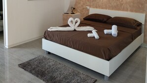 A modern bedroom with a large bed, a headboard with a textured design, a bedside table with a lamp, and a wall-mounted artwork. -  Agriturismo Heaven (Ricadi)