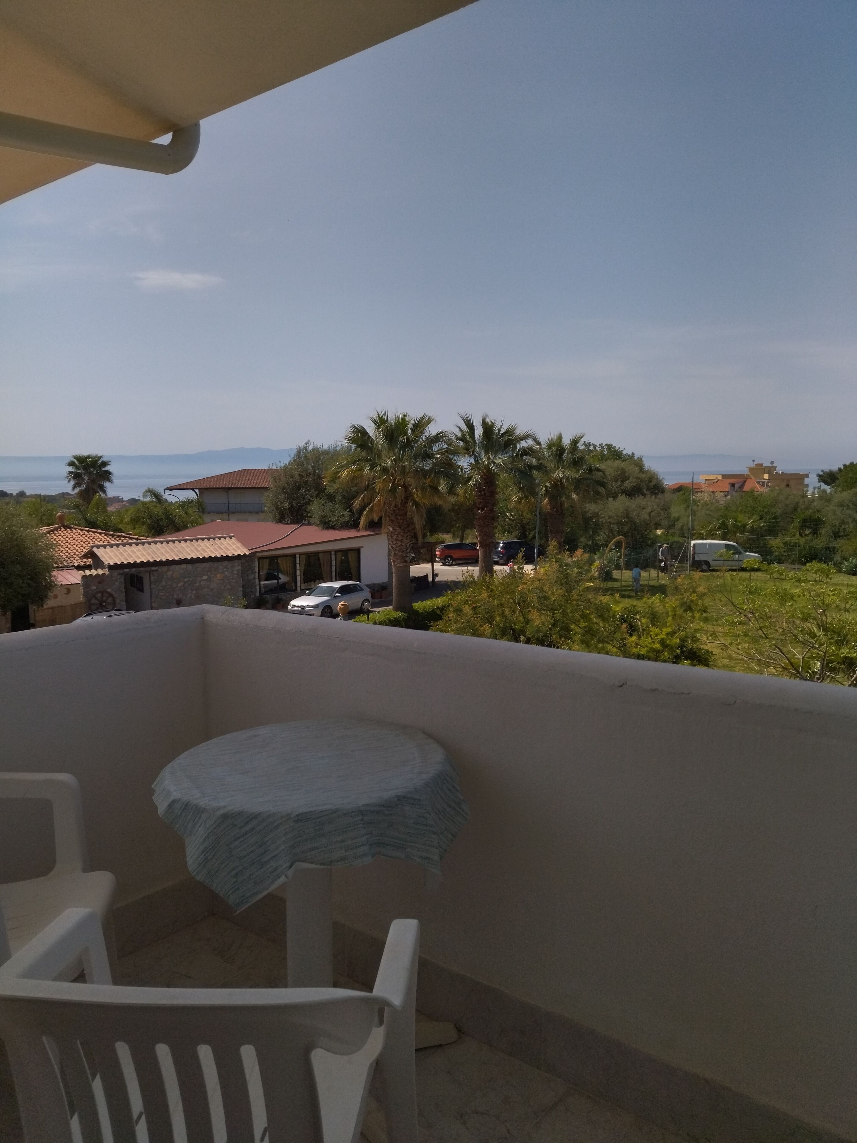 A balcony with a table and chairs, overlooking a residential area with houses, cars, and palm trees.