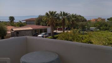 A balcony with a table and chairs, overlooking a residential area with houses, cars, and palm trees.