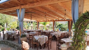 An outdoor restaurant with multiple tables and chairs, covered by a wooden roof, and surrounded by greenery. -  Agriturismo Heaven (Ricadi)