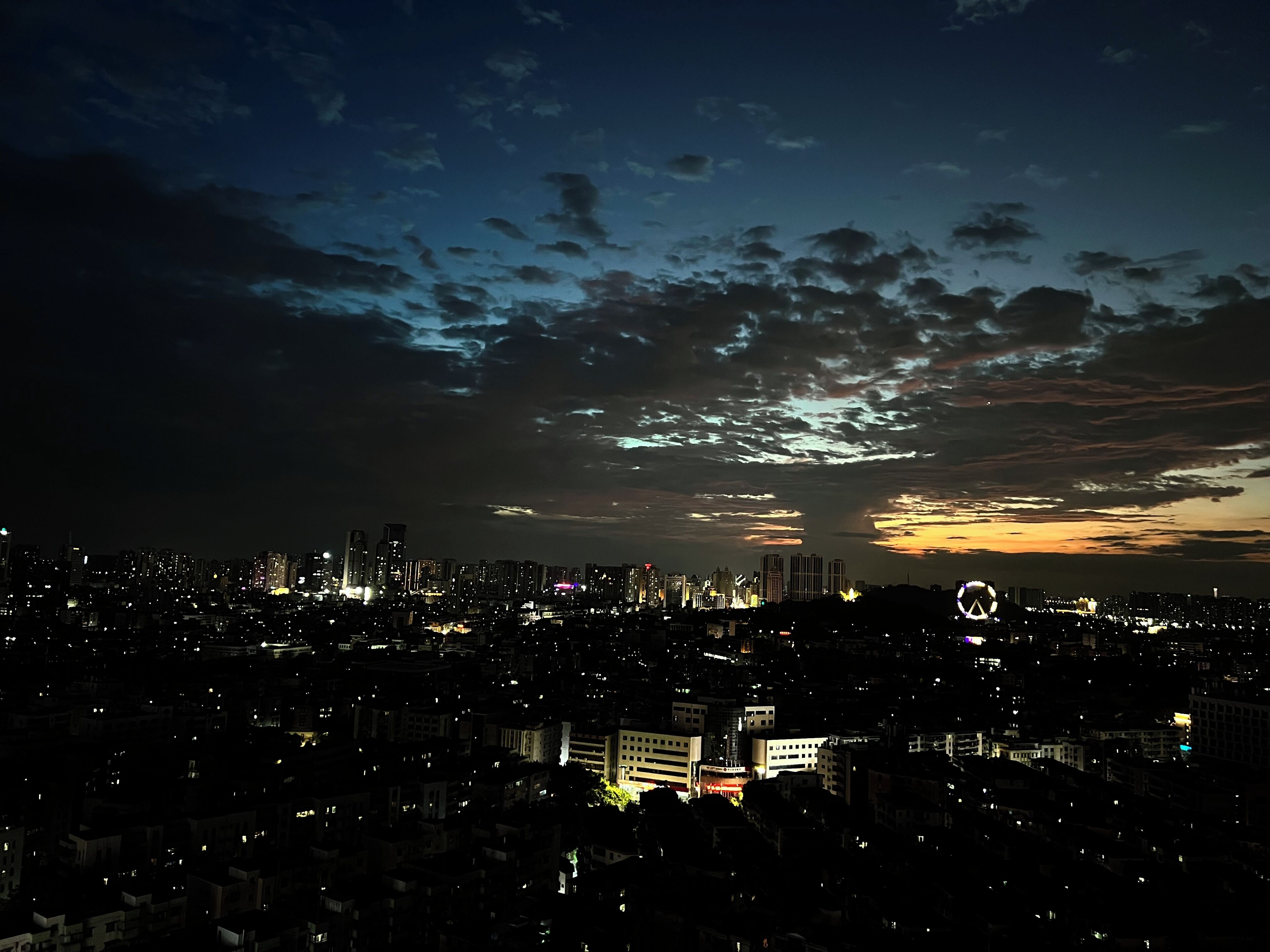 Une vue nocturne d’une ville, avec des bâtiments illuminés et un ciel nuageux.