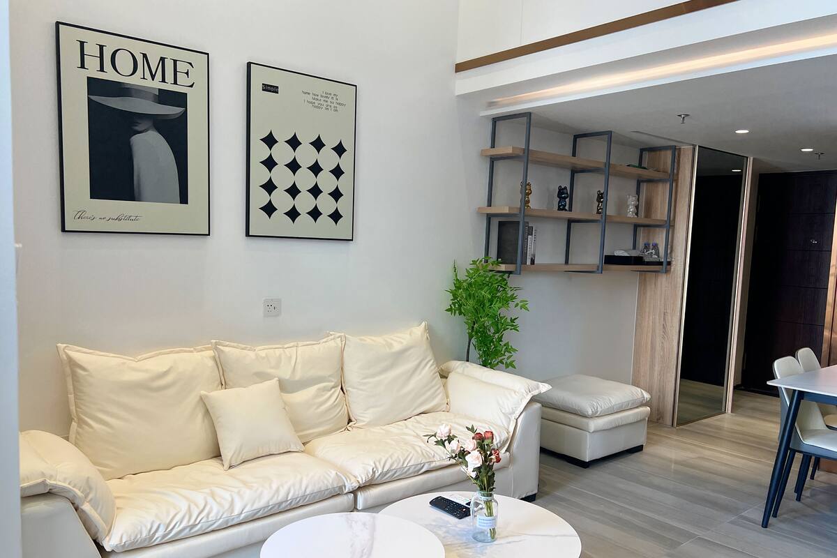 A modern living room with a beige leather sofa, two white round tables, and a small potted plant.
