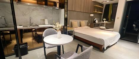 Ein modernes Hotelzimmer mit Bett, Schreibtisch und Stuhl. Ein kleiner Tisch mit Blumenvase steht dort. Das Zimmer verfügt über einen großen Spiegel und ein Fenster.