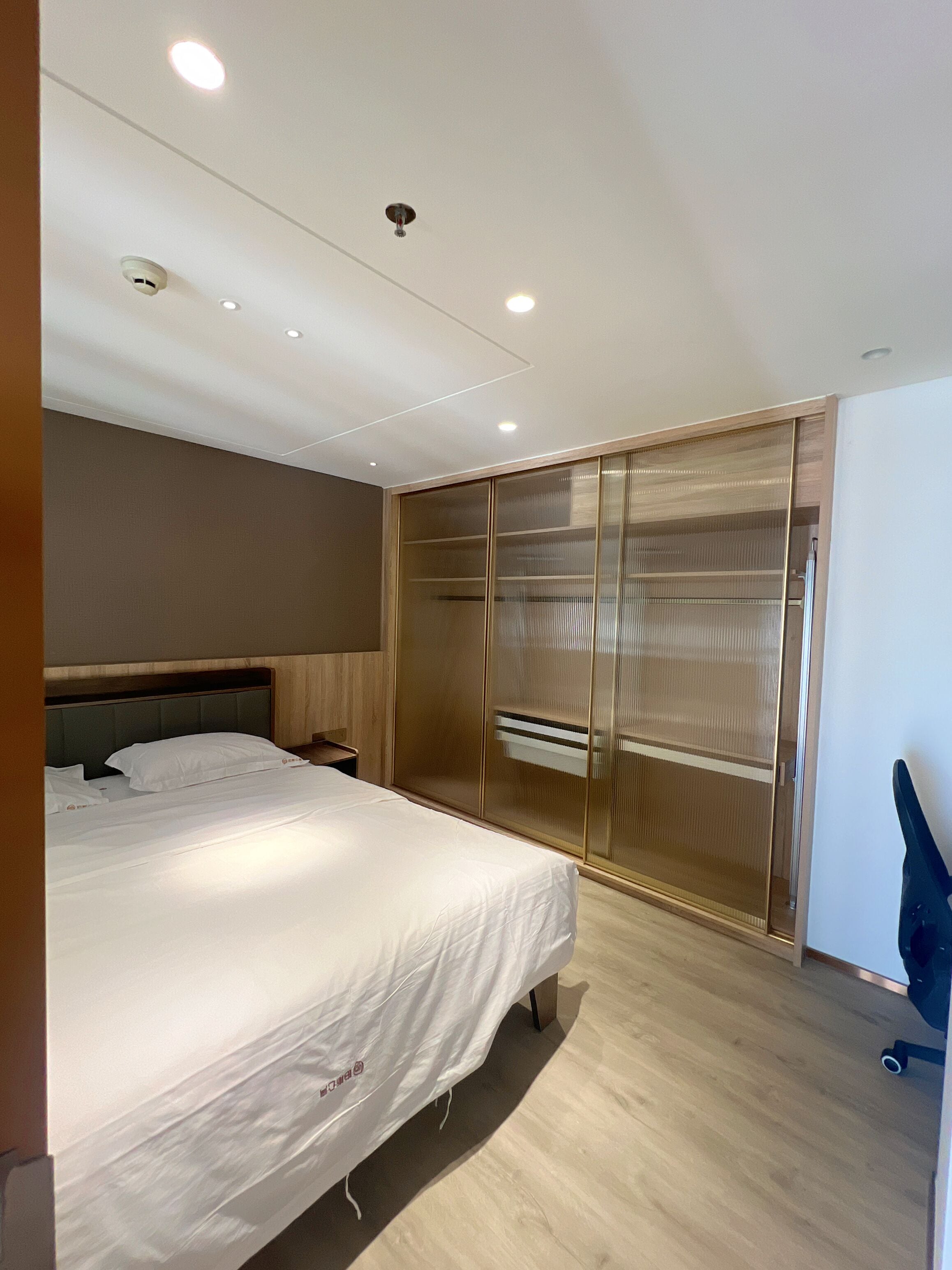 Un dormitorio moderno con una cama grande, un armario de madera con puerta espejada y luces empotradas en el techo.