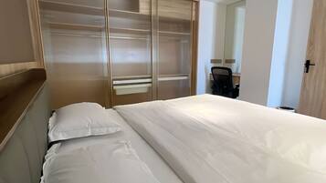 A modern hotel room with a large bed, a wooden headboard, a sliding glass door closet, and a desk with a chair.