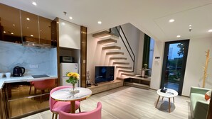 Un salon moderne avec un coin cuisine, une table à manger avec des chaises roses, un téléviseur et un escalier doté d’un éclairage intégré.