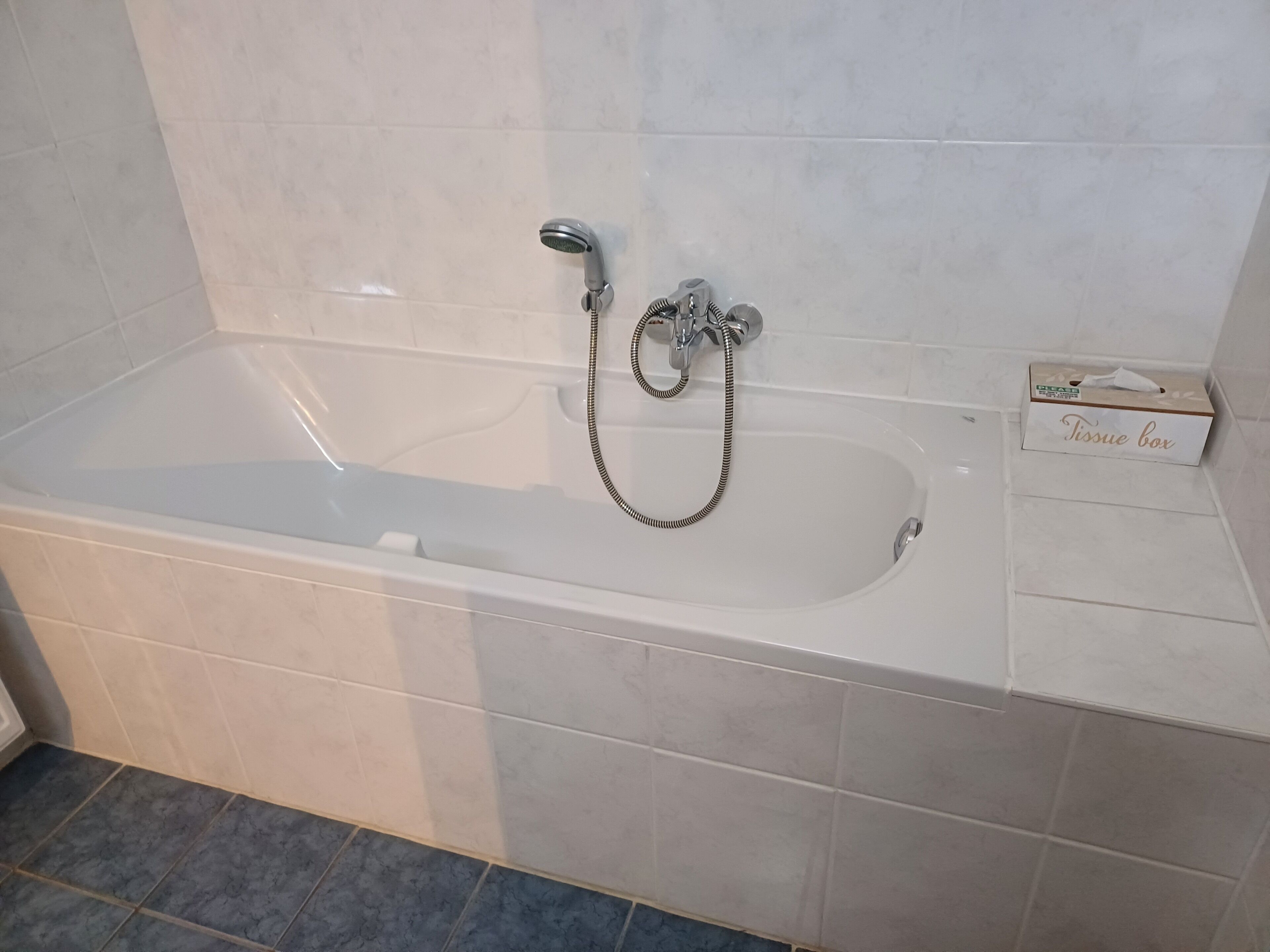 A modern bathroom with a bathtub, a handheld showerhead, and a tissue box on the side.