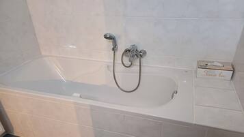A modern bathroom with a bathtub, a handheld showerhead, and a tissue box on the side.