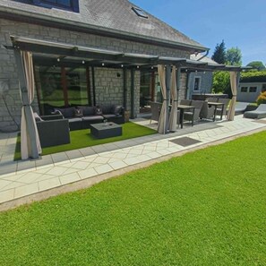 A covered outdoor seating area with a stone wall, a sofa, and a table.