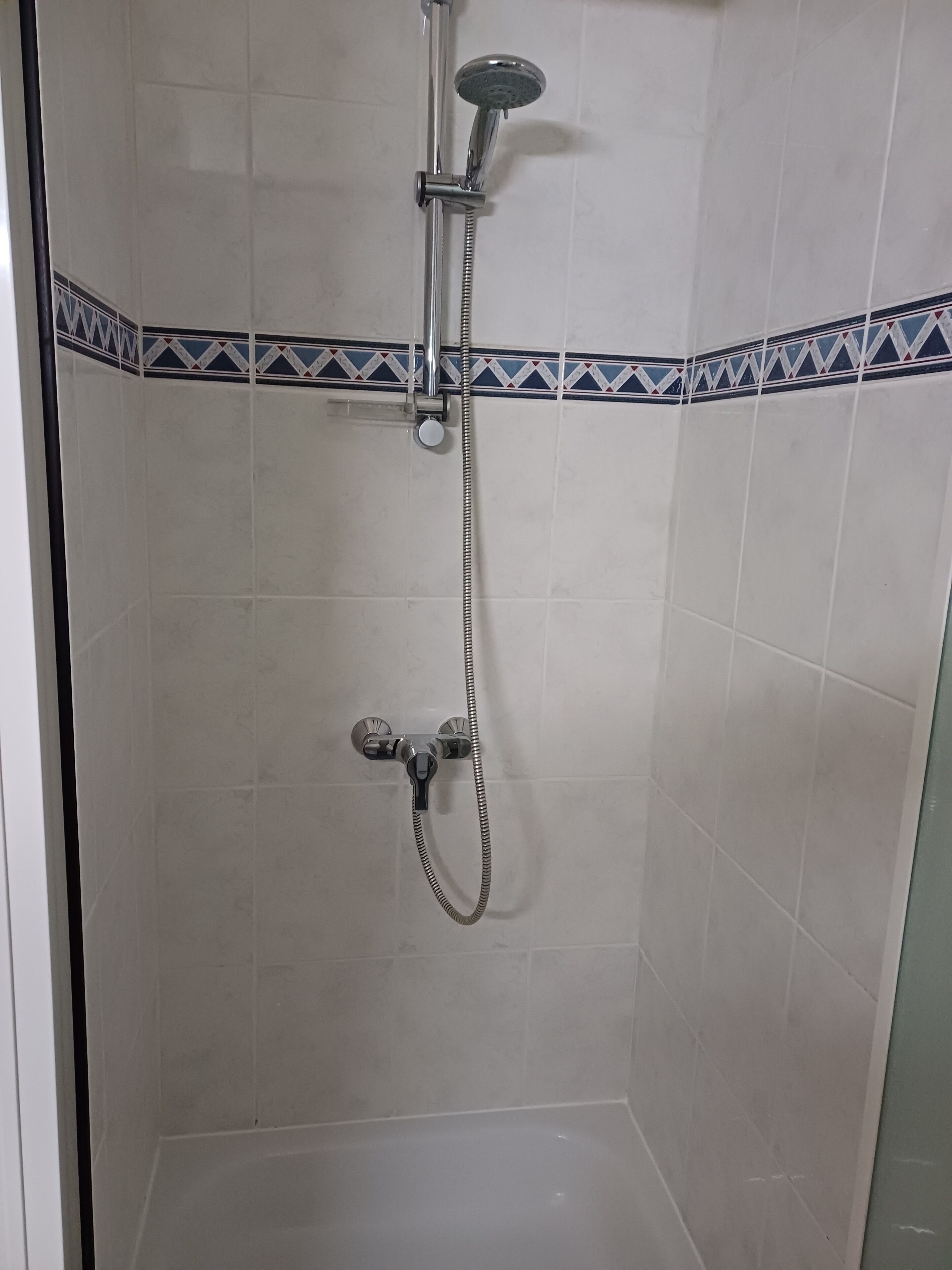 Douchegedeelte met een handdouche en een hoofddouche, beide bevestigd aan een wand met decoratieve tegels.