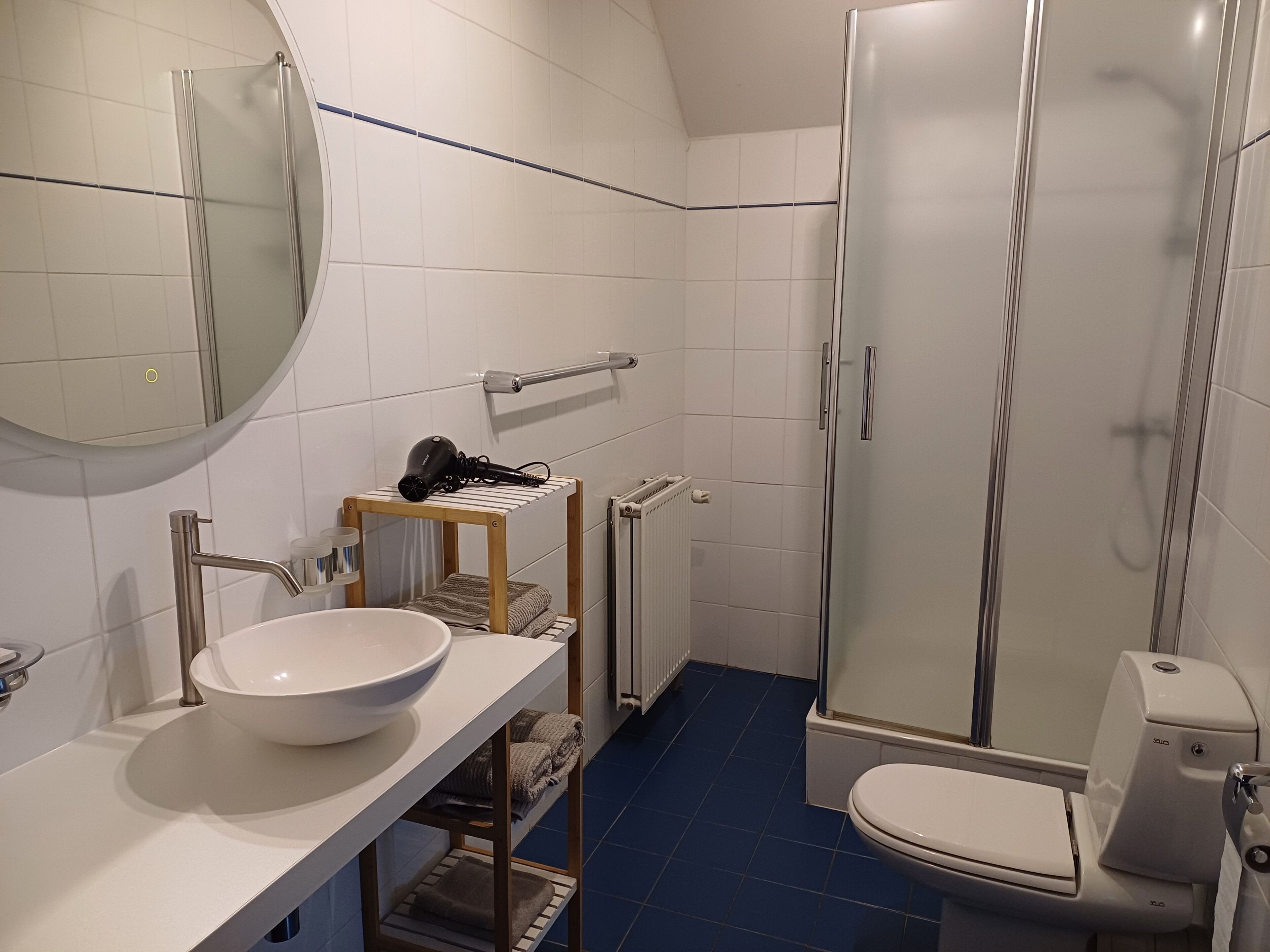 Un baño con lavamanos blanco, un espejo, toallero, ducha e inodoro.