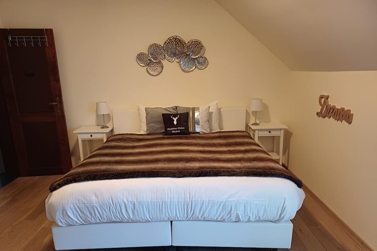A bedroom with a large bed, two bedside tables with lamps, a decorative wall piece, and a sign on the wall.
