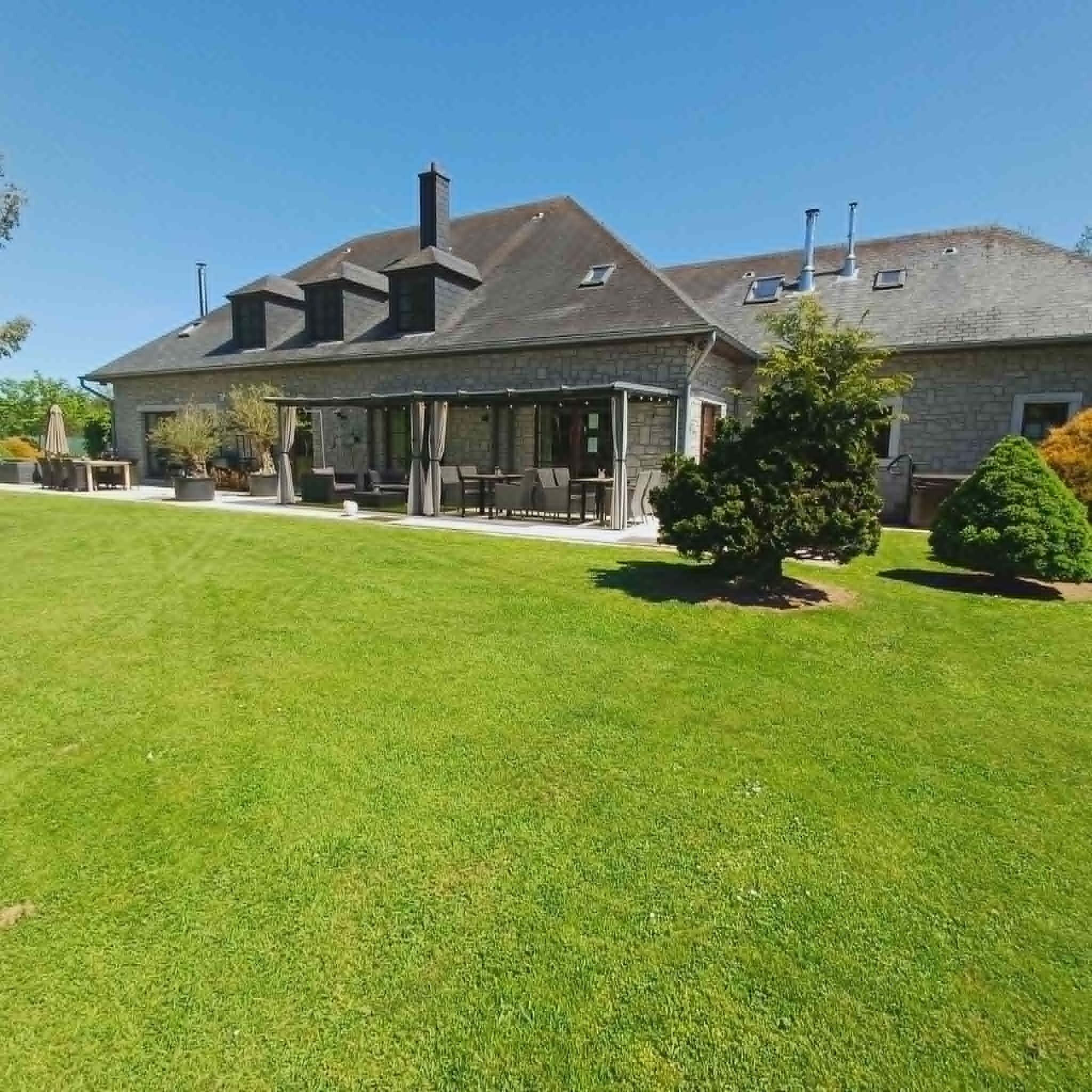 A stone house with a covered patio and a well-maintained lawn.