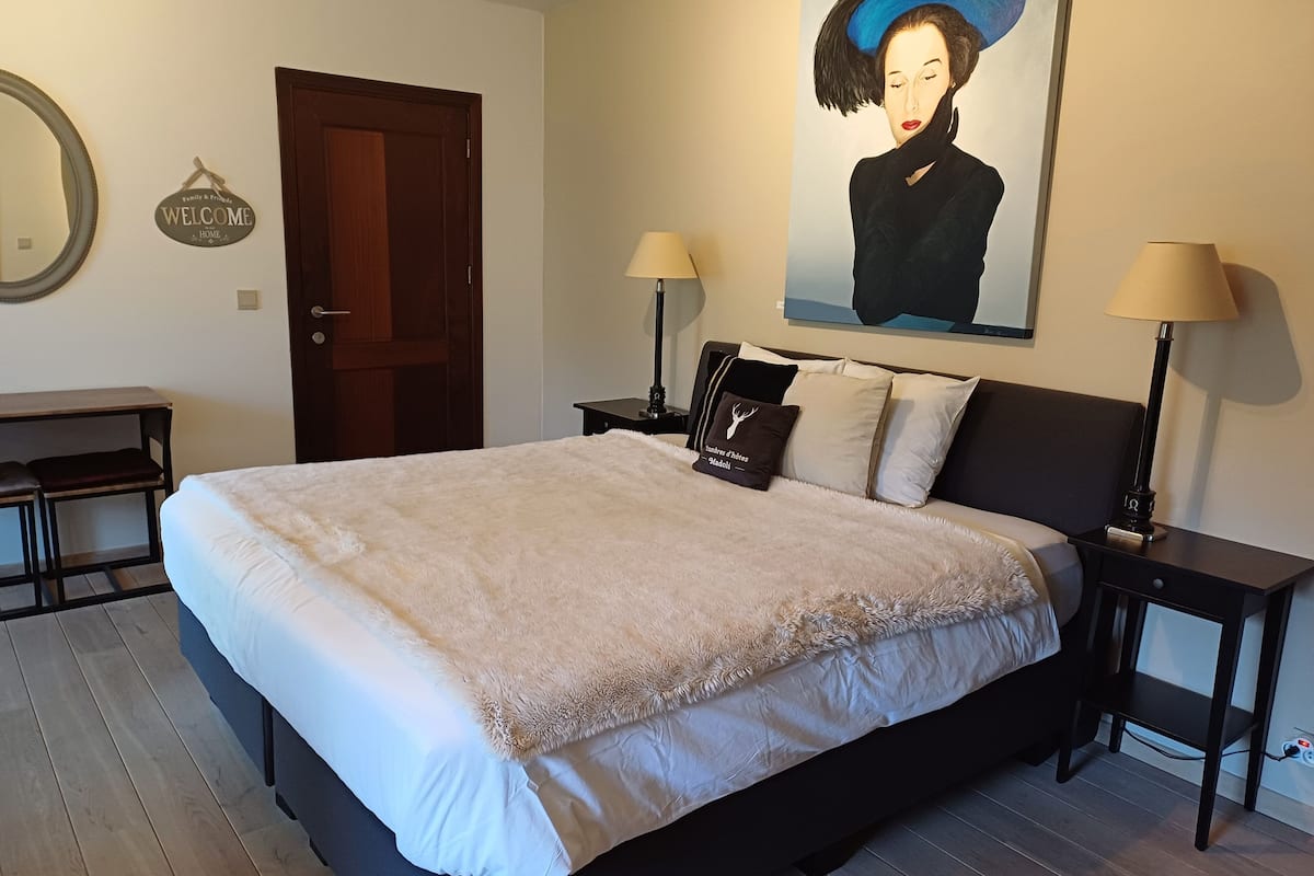 A neatly arranged bedroom with a large bed, two bedside tables with lamps, a desk, and a door.