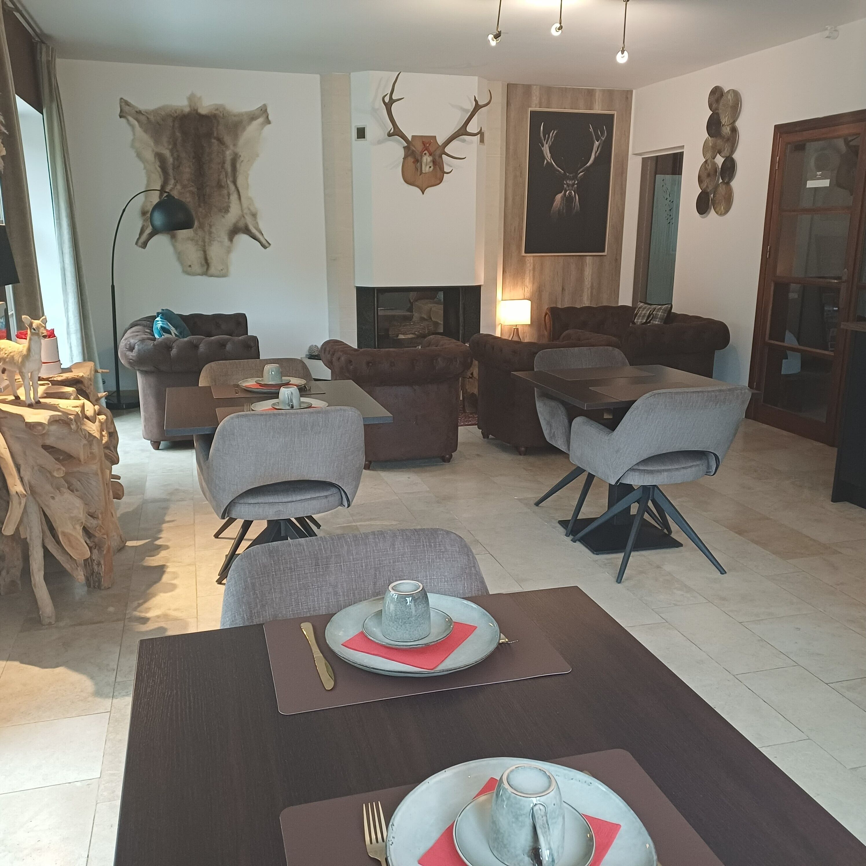 Un soggiorno moderno con camino, divani in pelle, un tavolo da pranzo apparecchiato per due e teste di animali appese alle pareti.