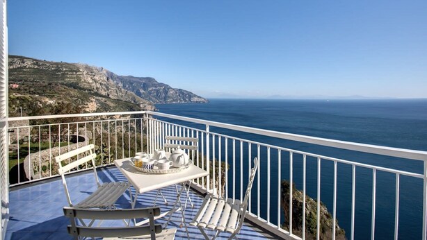A balcony with a table set for two, overlooking a coastal landscape.