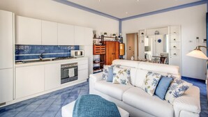 A modern kitchen with white cabinets, a blue backsplash, and a white sofa with patterned cushions.