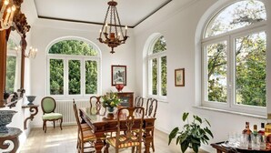 A dining room with a wooden table and chairs, large arched windows, and a chandelier. - Casa Bianca in Massa Lubrense (Massa Lubrense)