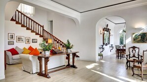 A spacious living area with a wooden staircase, a sofa with colorful cushions, a dining table, and a chandelier. - Casa Bianca in Massa Lubrense (Massa Lubrense)
