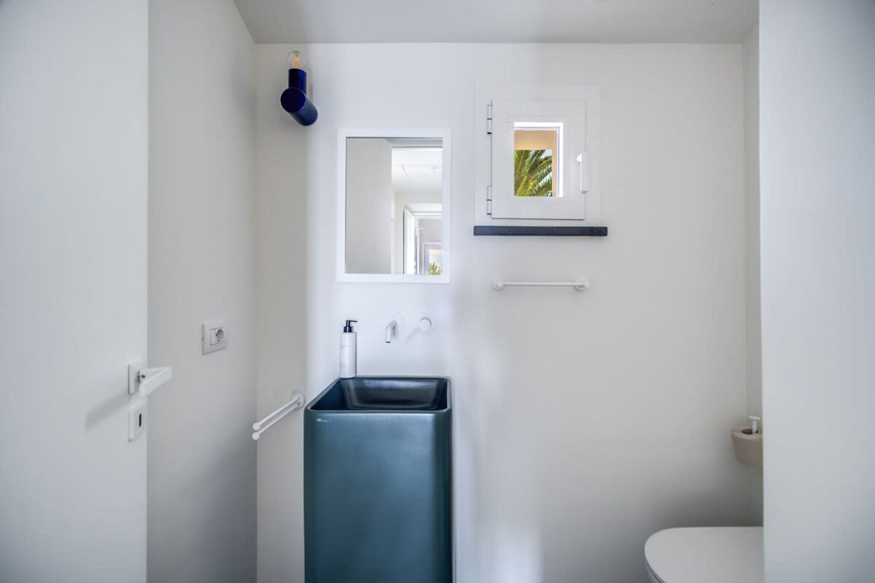 Une salle de bain moderne avec un lavabo rectangulaire, une petite fenêtre et des toilettes blanches.