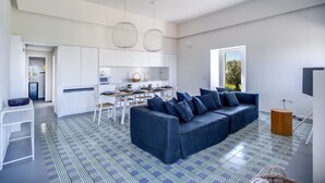 A modern living room with a blue sofa, a dining table, and a kitchen in the background. - Casa del Capitano in Termini (Massa Lubrense)