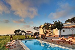 A pool area with lounge chairs, a pergola, and a building with a white facade.