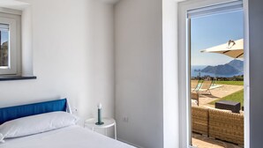 A bedroom with a bed, a nightstand, and a view of an outdoor patio with a pool and lounge chairs. - Casa del Capitano in Termini (Massa Lubrense)