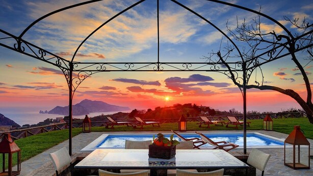 A poolside area with a gazebo, lounge chairs, and a table with a fruit basket. - Casa del Capitano in Termini (Massa Lubrense)