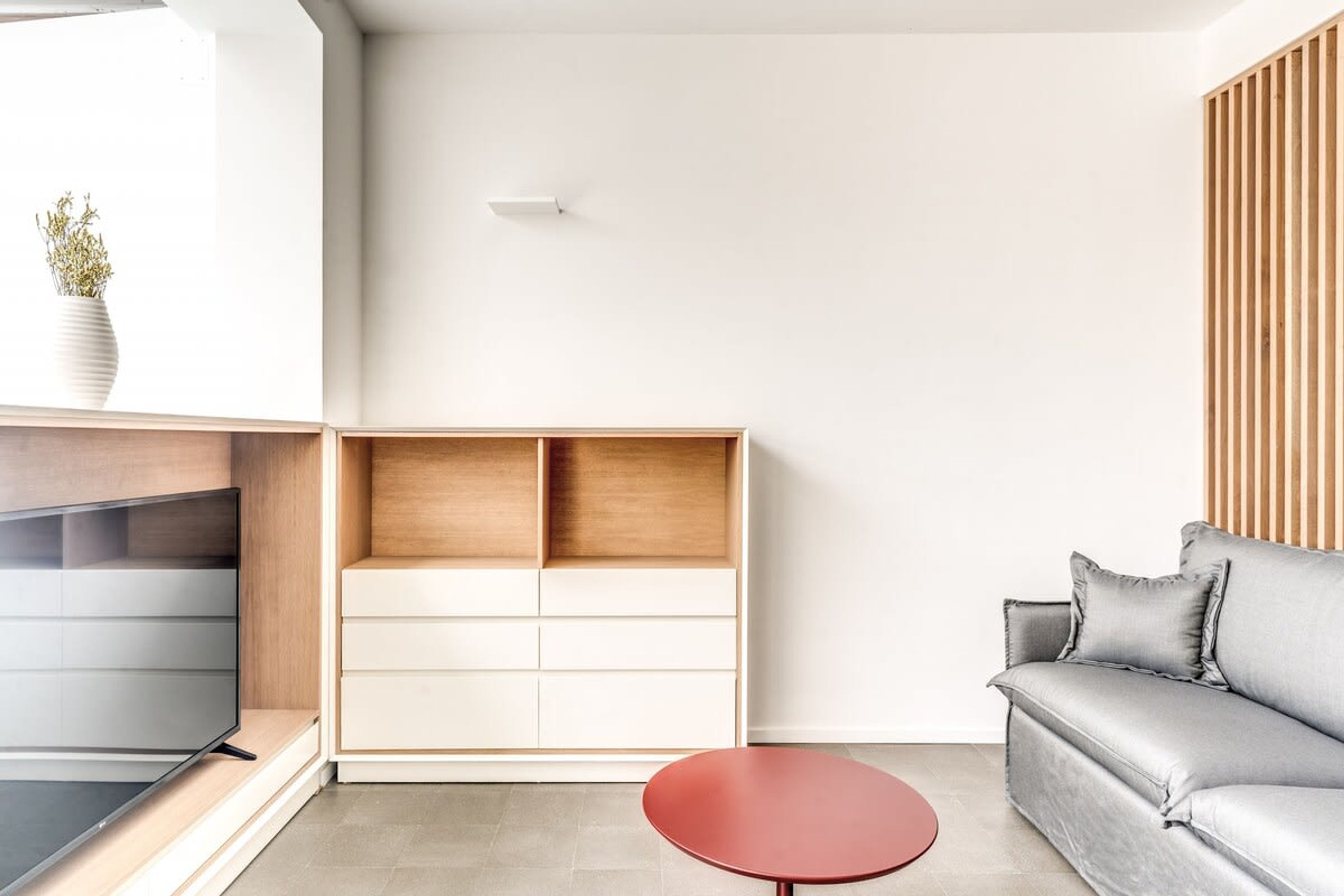 A modern living room with a grey sofa, a red table, and a wooden cabinet with drawers.