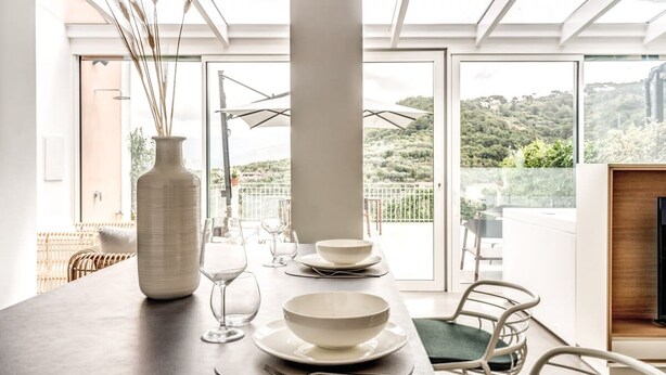 A dining area with a table set for two, a vase, and a view of a balcony with a railing and greenery. - Suite La Panoramica in Sant Agata sui Due Golfi (Massa Lubrense)