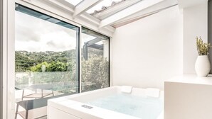 A modern bathroom with a large bathtub, a glass-enclosed shower area, and a view of a lush garden. - Suite La Panoramica in Sant Agata sui Due Golfi (Massa Lubrense)