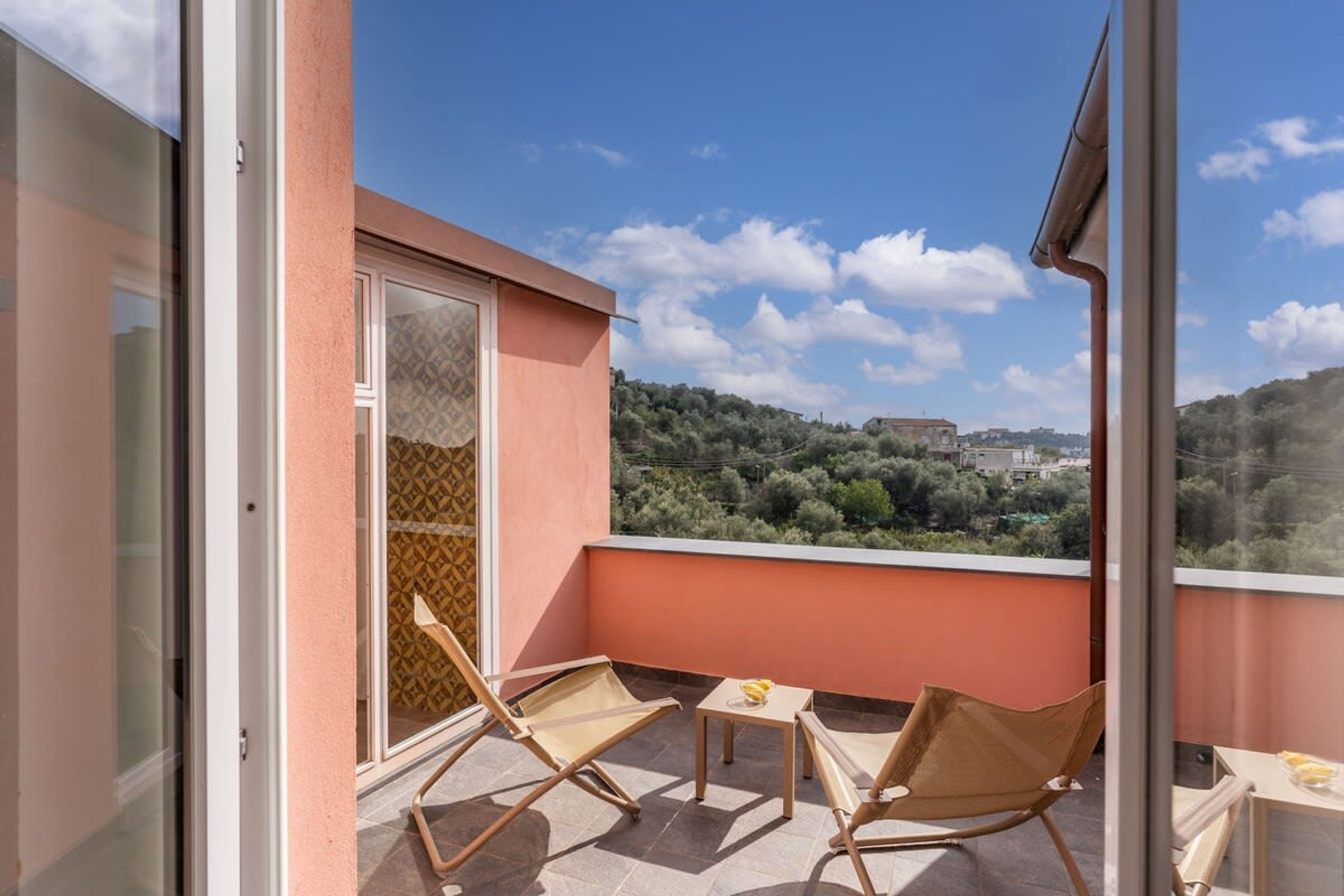 A balcony with two chairs and a small table, overlooking a scenic landscape with trees and buildings.