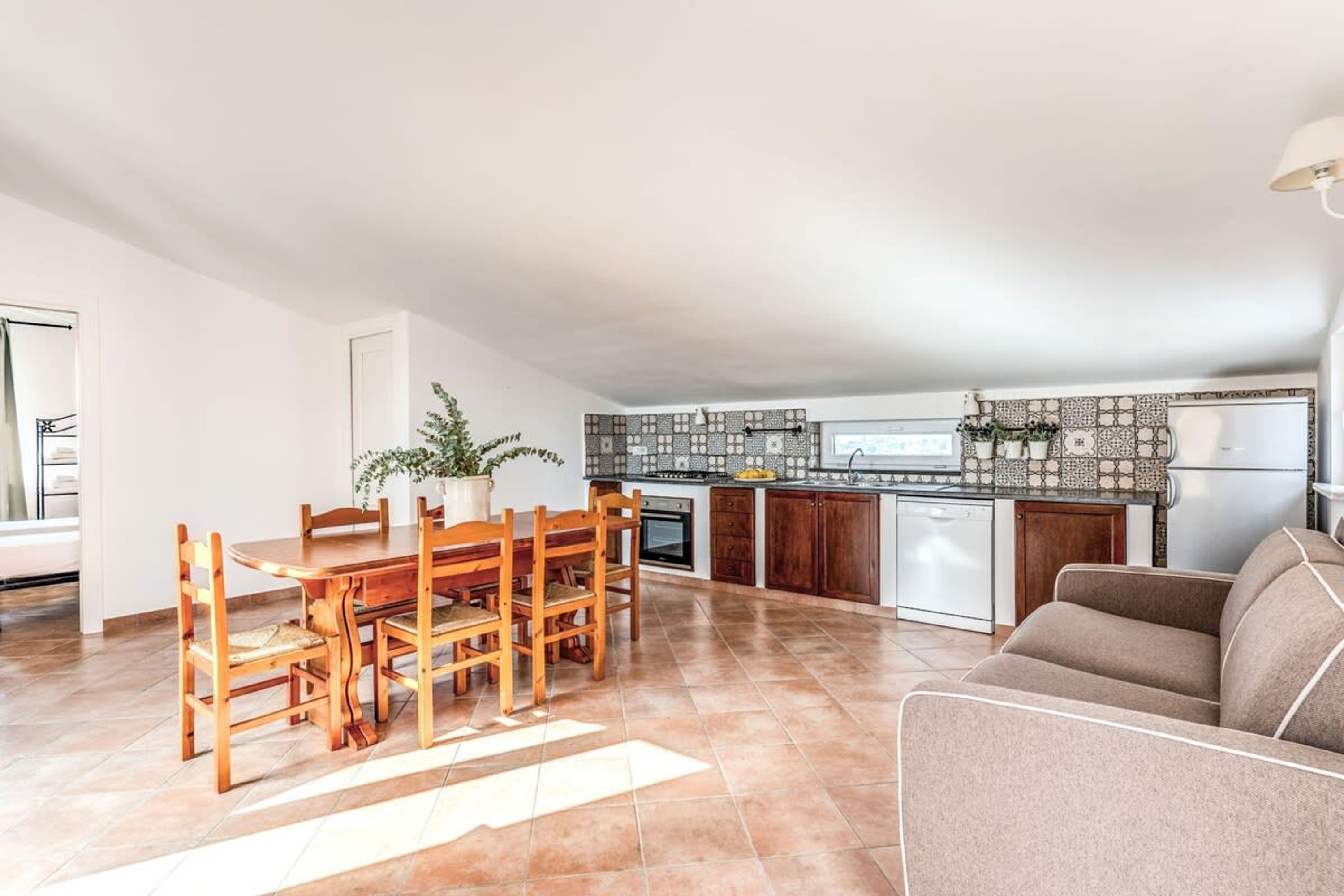 Une cuisine spacieuse avec un coin repas, comprenant une table et des chaises en bois, un canapé et une plante en pot.