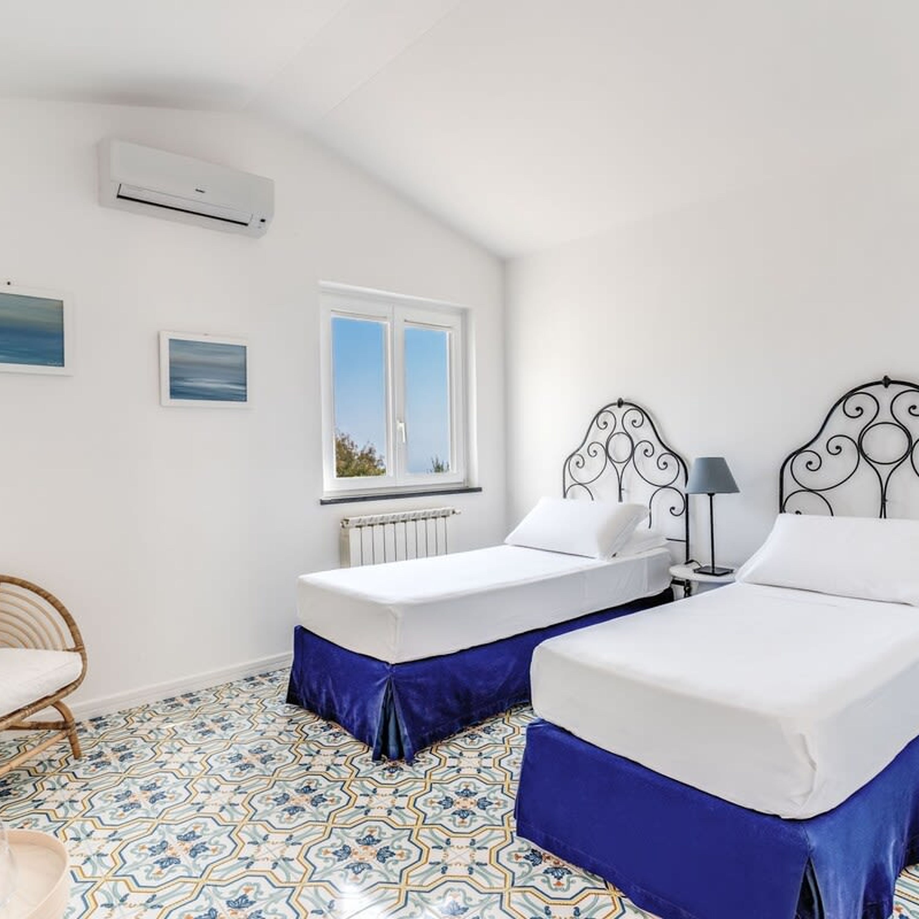 A room with two beds, a radiator, a window, and a patterned floor.