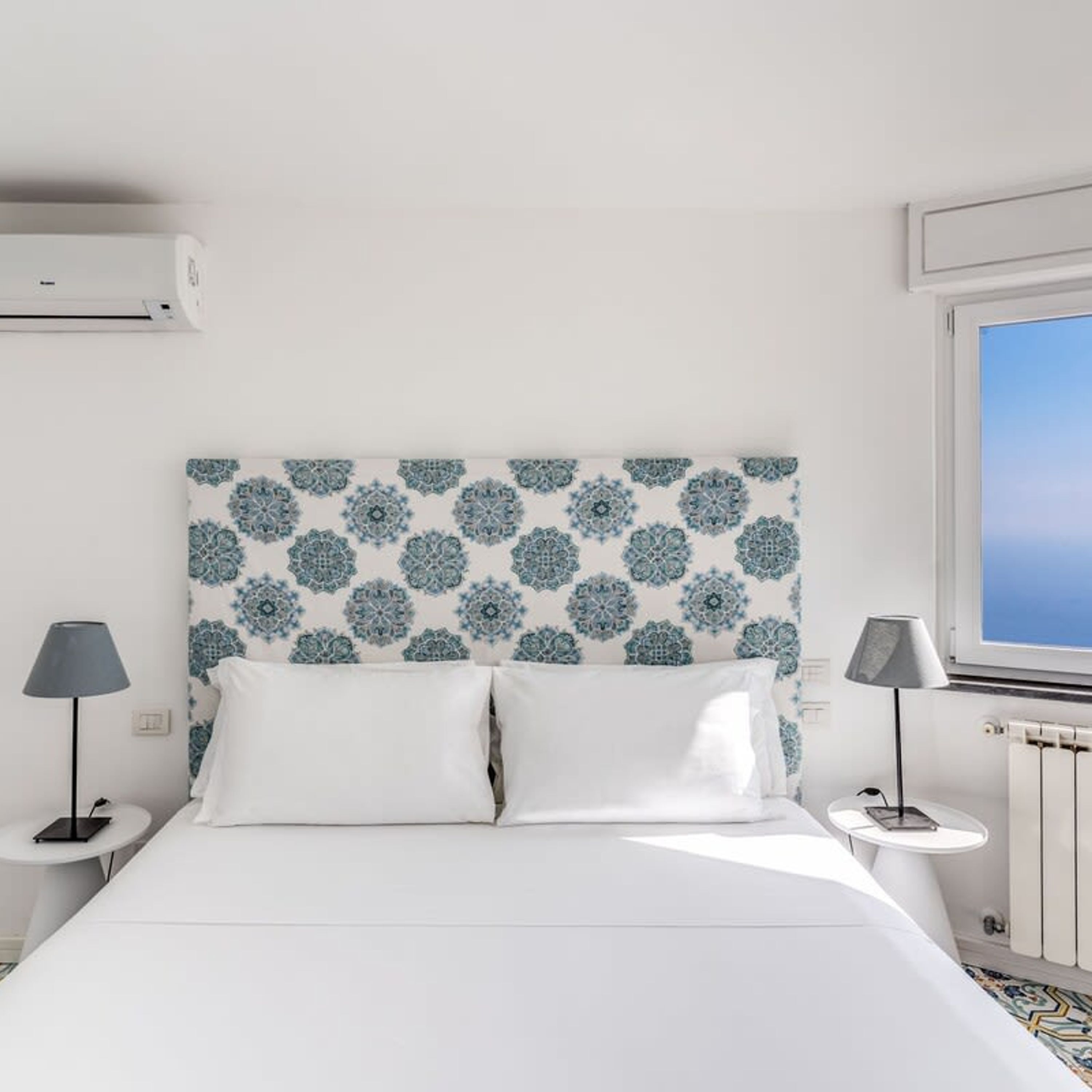 A modern bedroom with a patterned headboard, white bedding, and two bedside tables with lamps.