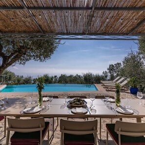An outdoor dining area with a pool view, tables set with wine glasses and plates, and chairs.