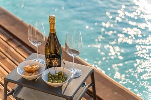 Ein Tisch mit einer Champagnerflasche, zwei Gläsern, einer Oliven-Schale und einer Schale Kekse am Poolrand.