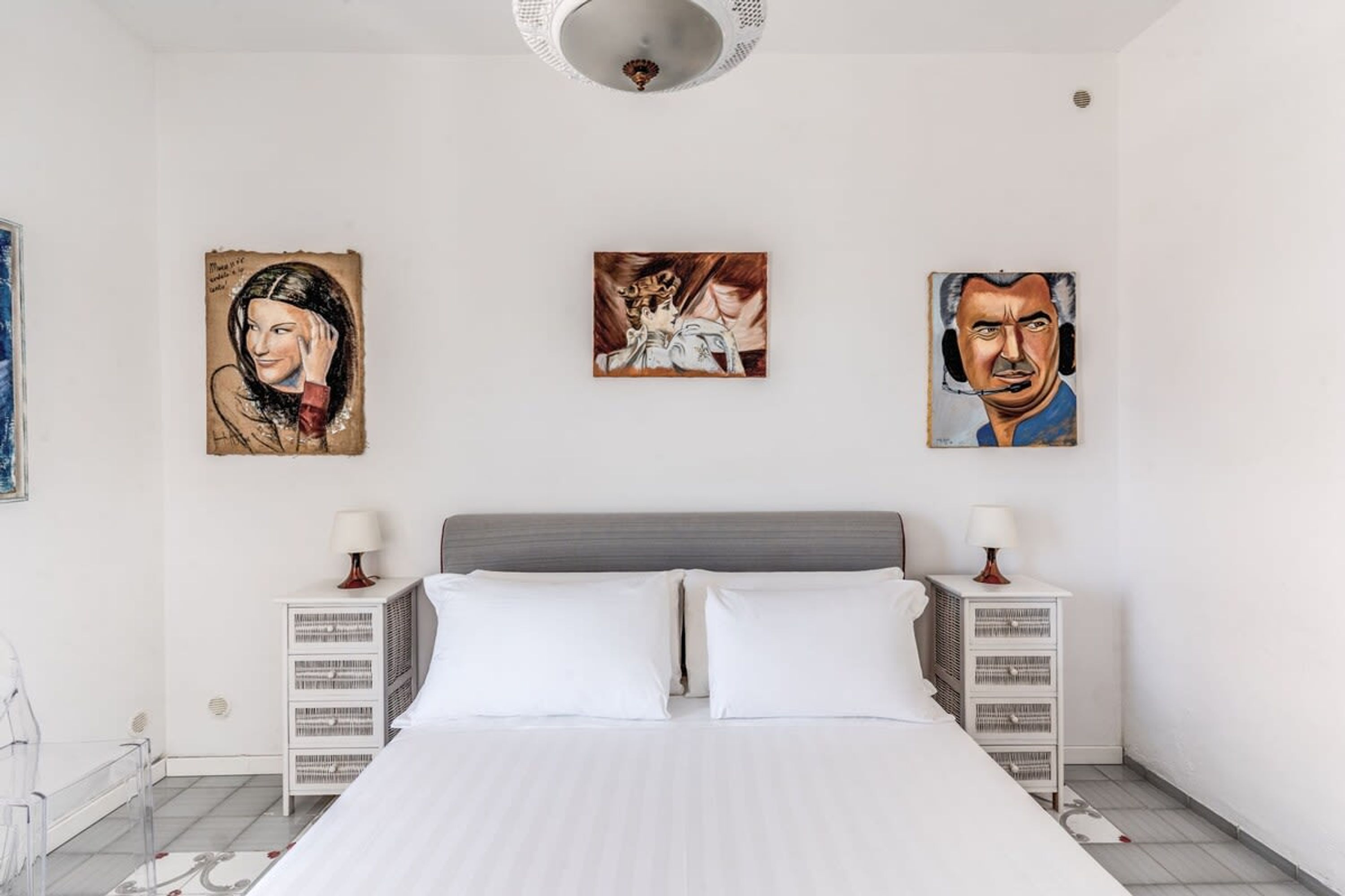 A hotel room with a large bed, two bedside tables with lamps, and three paintings on the wall.