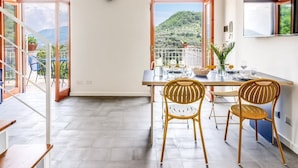 Un coin repas avec une table dressée pour quatre personnes, deux chaises en osier et une vue sur un paysage montagneux grâce à de grandes fenêtres.