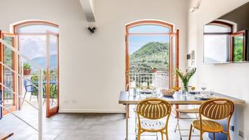 Comedor con una mesa dispuesta para cuatro, dos sillas de mimbre y vistas a un paisaje montañoso a través de ventanas amplias.