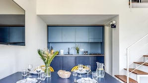 Un coin repas avec une table bleue et des chaises jaunes, une cuisine avec des meubles bleus et un escalier.